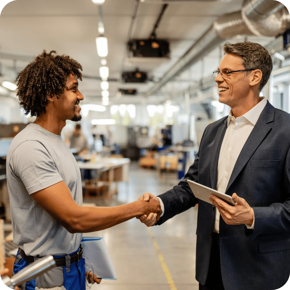 Deux hommes se serrent la main dans un atelier industriel, l’un en costume tenant une tablette - Illustration d’une relation de confiance entre un chef d’entreprise et son conseiller pour anticiper un contrôle fiscal en toute sérénité.