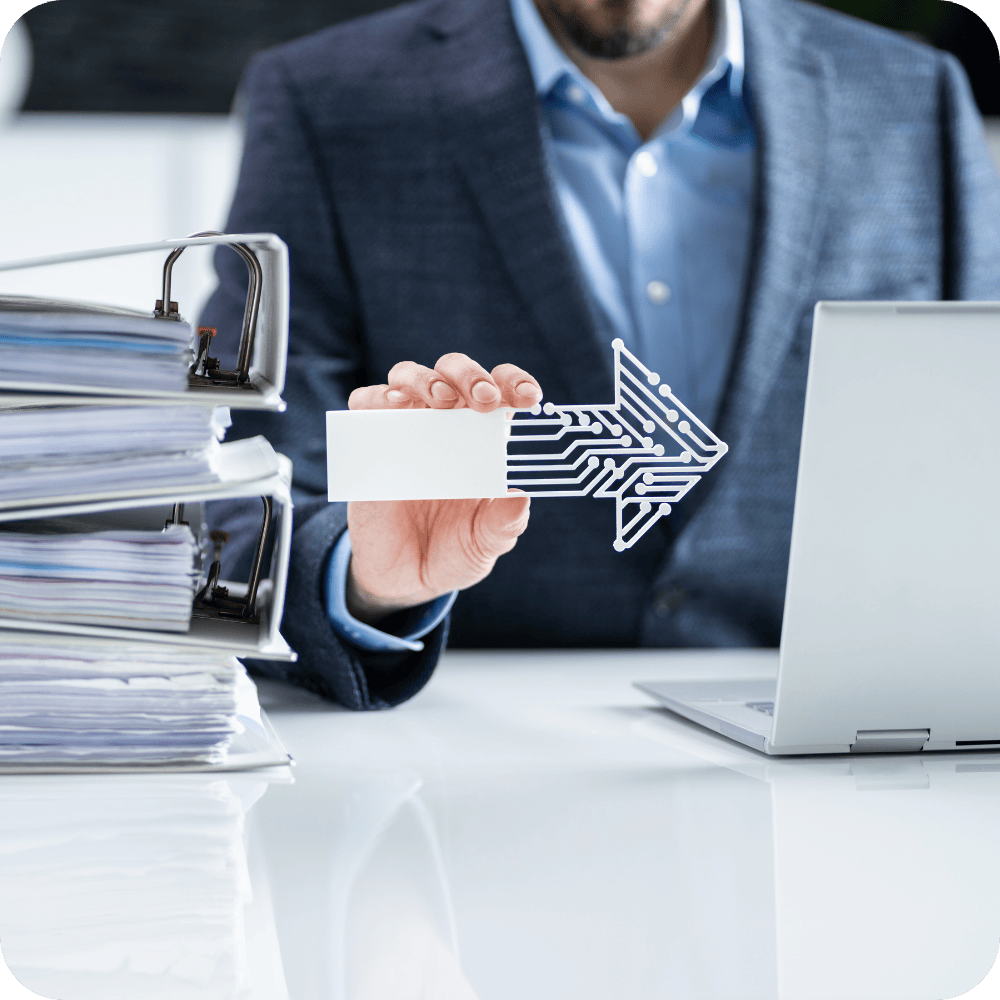 Un homme en costume tenant une flèche digitale en direction d’un ordinateur portable, avec une pile imposante de classeurs papier à ses côtés. L’image symbolise le passage de la gestion administrative traditionnelle à la digitalisation des processus. Elle illustre les enjeux de la transformation digitale en entreprise et l’importance de la conduite du changement pour mobiliser les équipes, automatiser les tâches chronophages et gagner en performance opérationnelle.