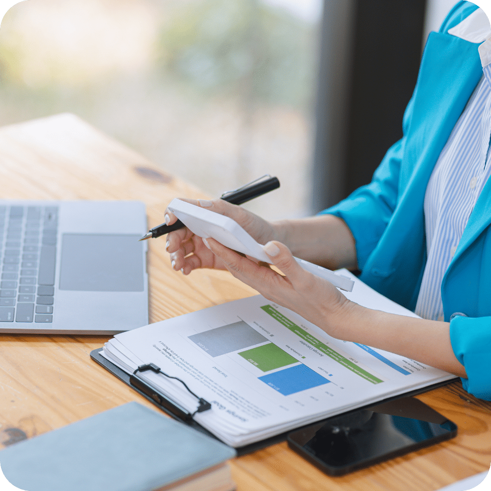 Professionnelle analysant des graphiques financiers sur un rapport papier, ordinateur portable et smartphone à portée de main - Illustration de l’utilisation stratégique des données comptables pour piloter la performance de l’entreprise.