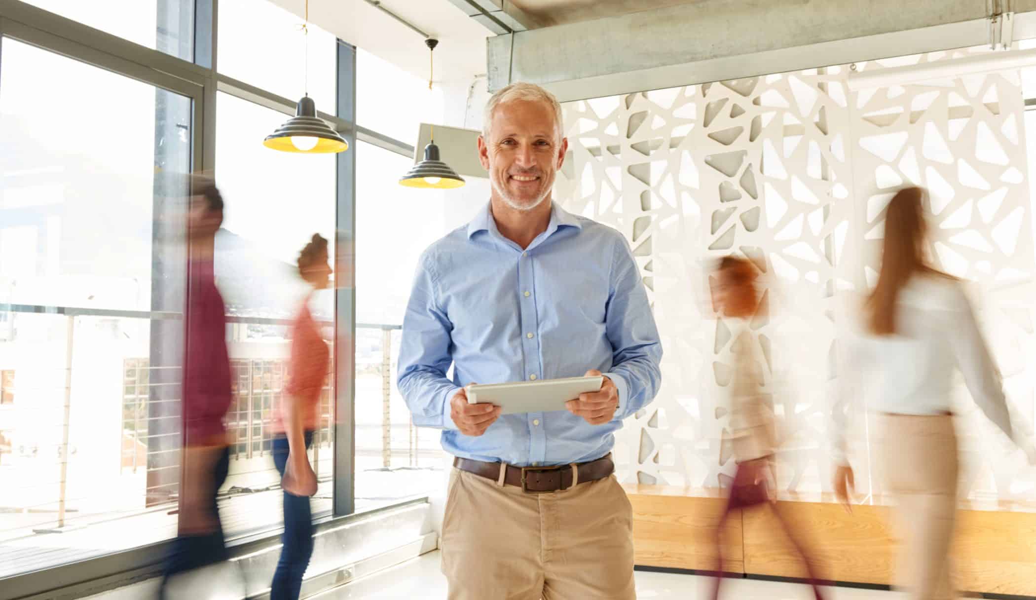 Dirigeant d’entreprise souriant tenant une tablette numérique dans un espace moderne – pilotage d’activité, analyse des indicateurs comptables et accompagnement stratégique pour artisans et commerçants.

