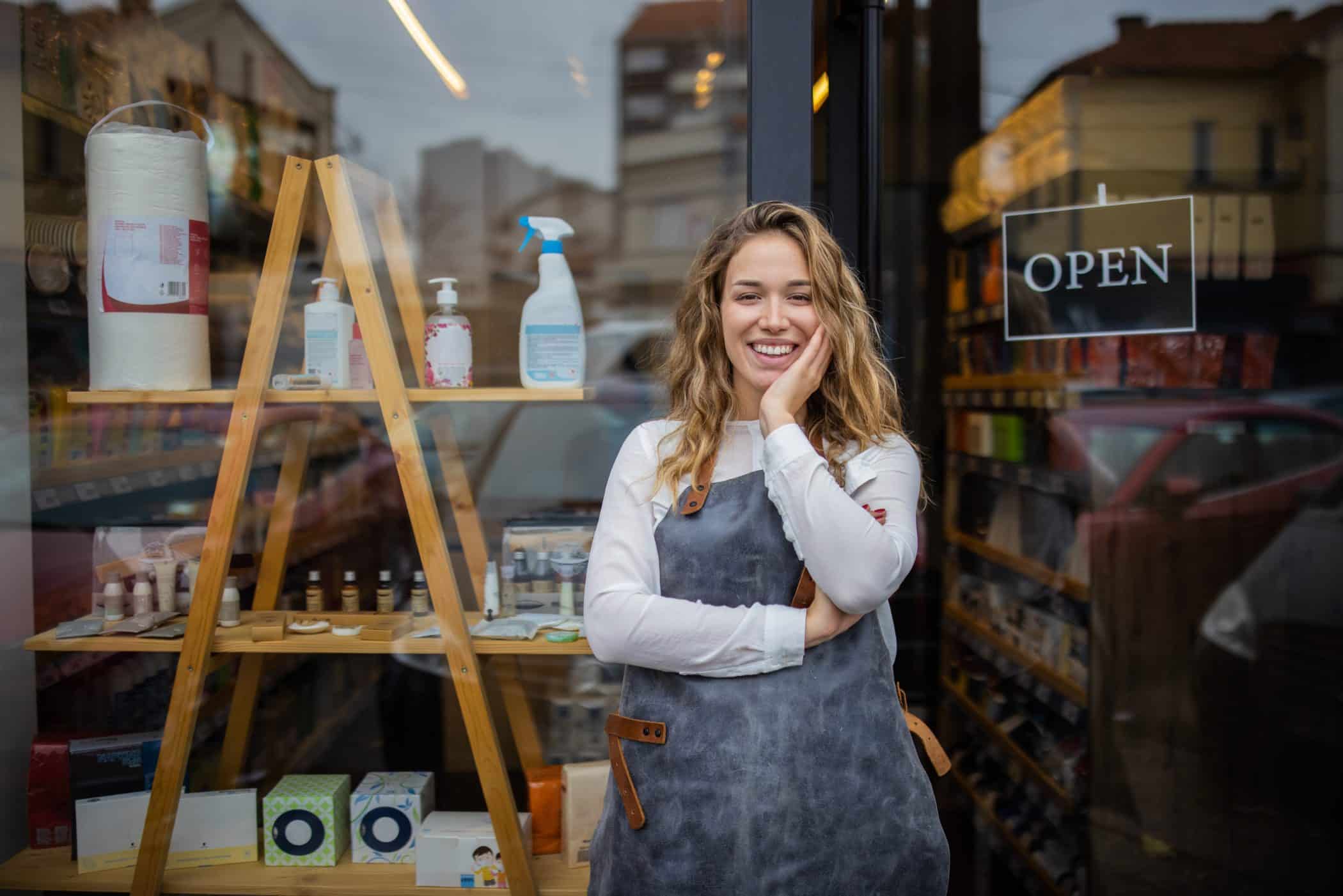 Commerçante souriante devant sa boutique de proximité – stratégies pour booster sa visibilité locale, attirer de nouveaux clients et développer son chiffre d’affaires en commerce de détail.

